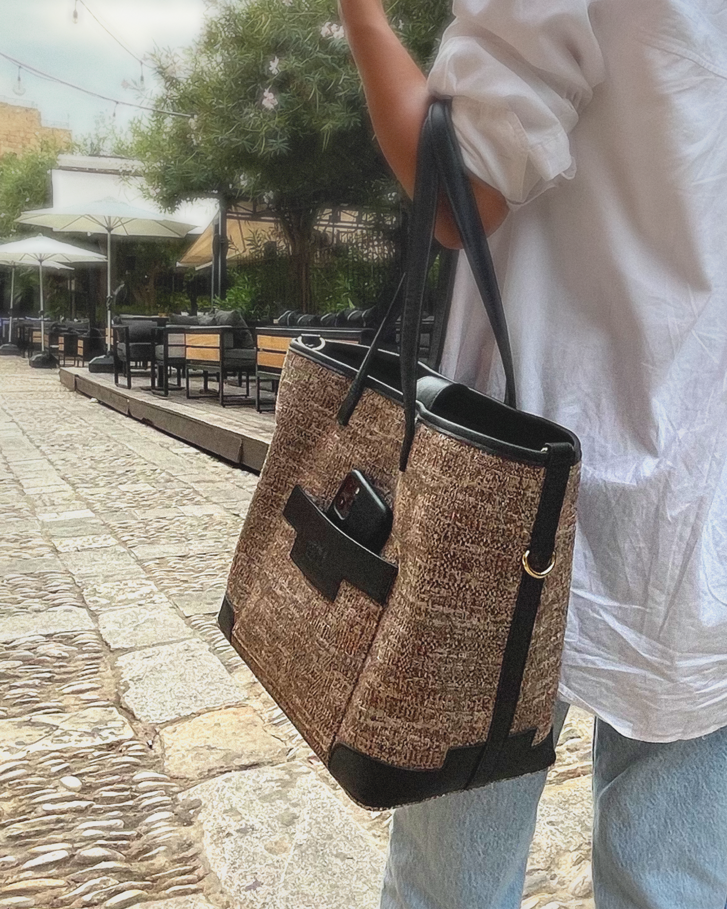 Person holding a woven large tote bag on a stone pavement