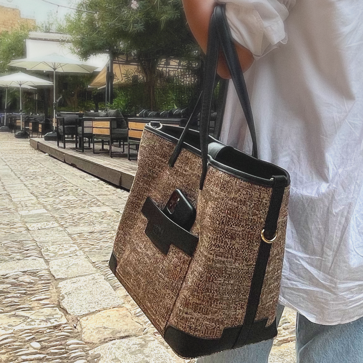 Person holding a woven large tote bag on a stone pavement
