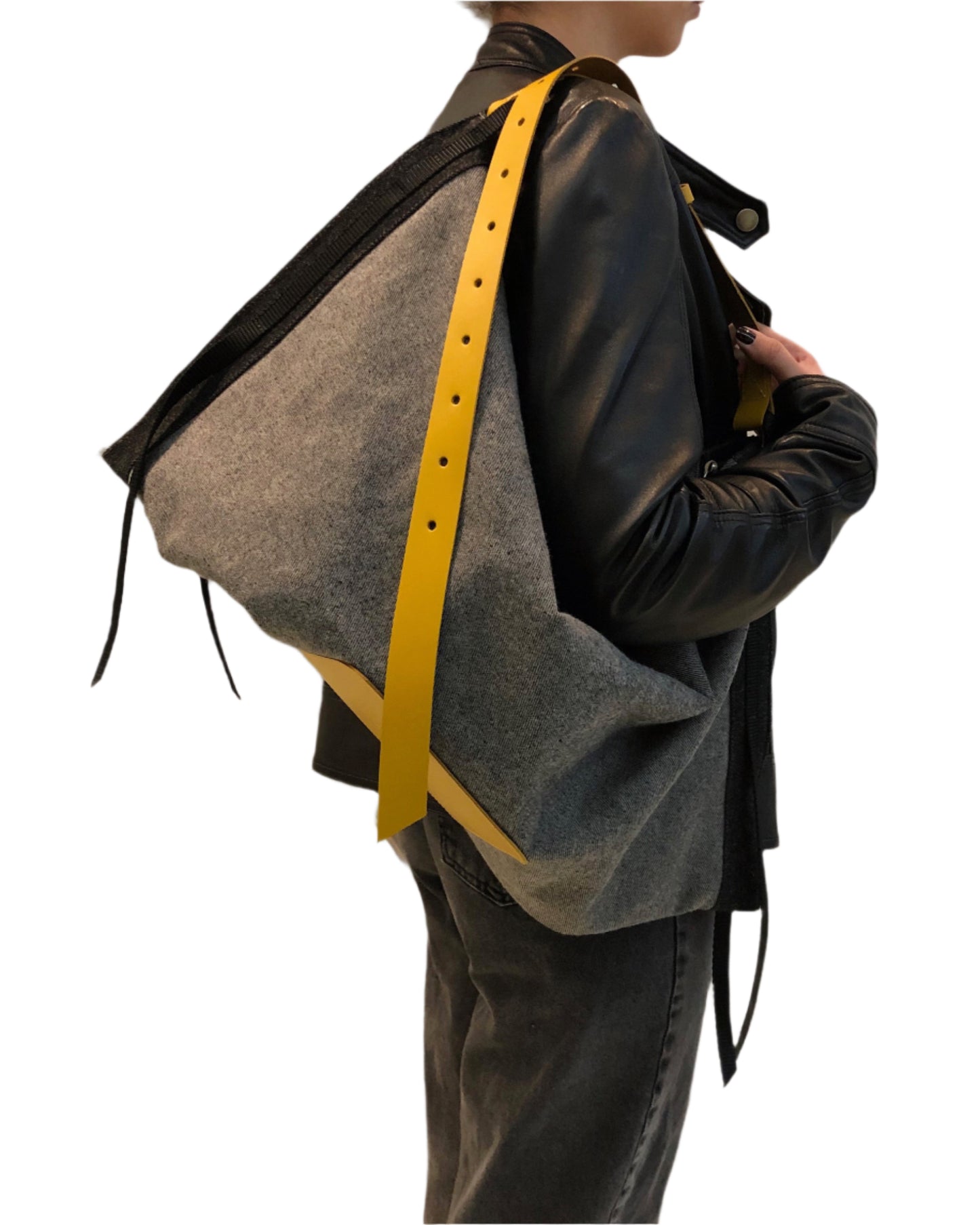 Person wearing a dark jacket with a gray denim bag over one shoulder and a mustard color leather strap.