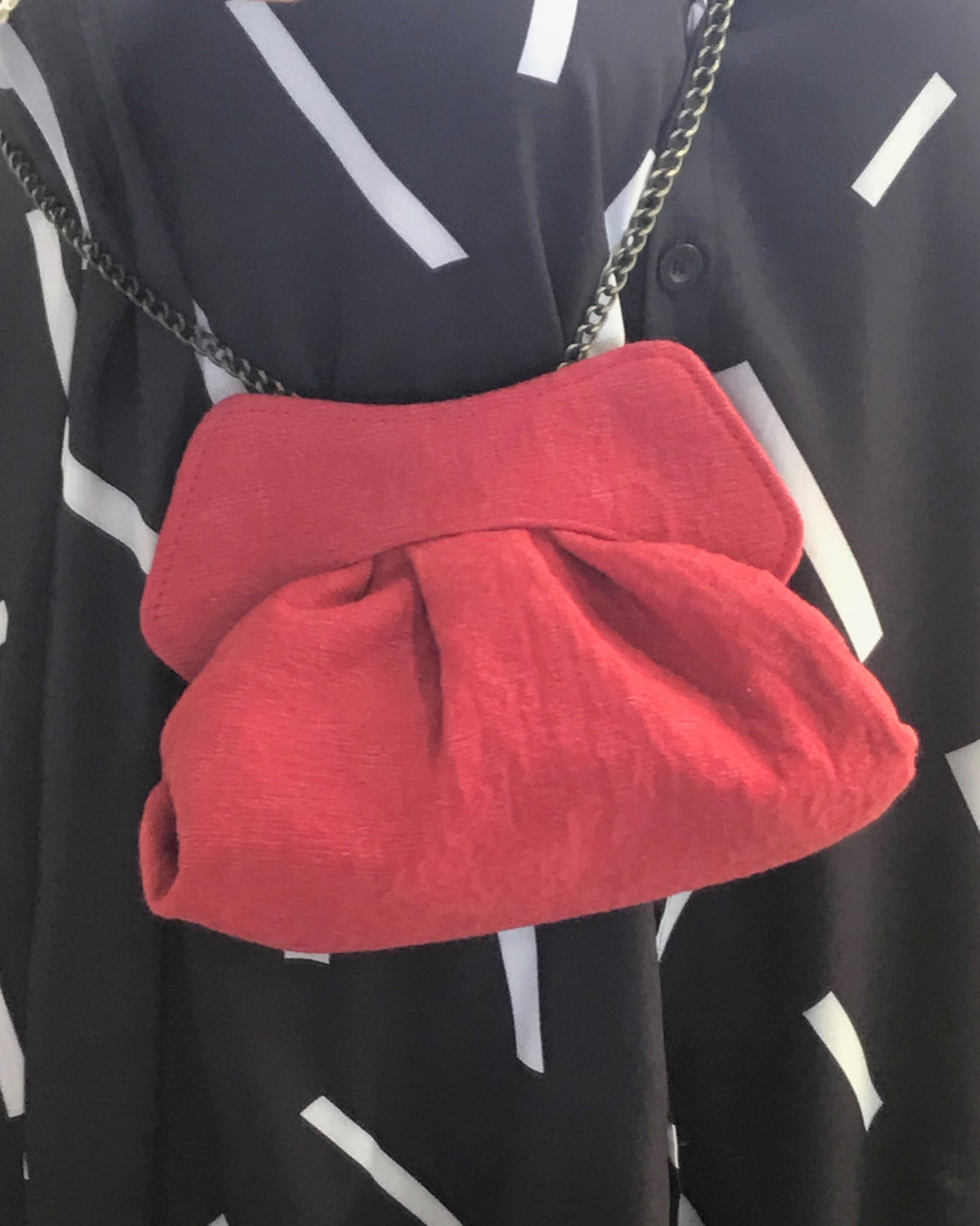 Red clutch worn over one shoulder by a person wearing a black dress with white patterns.