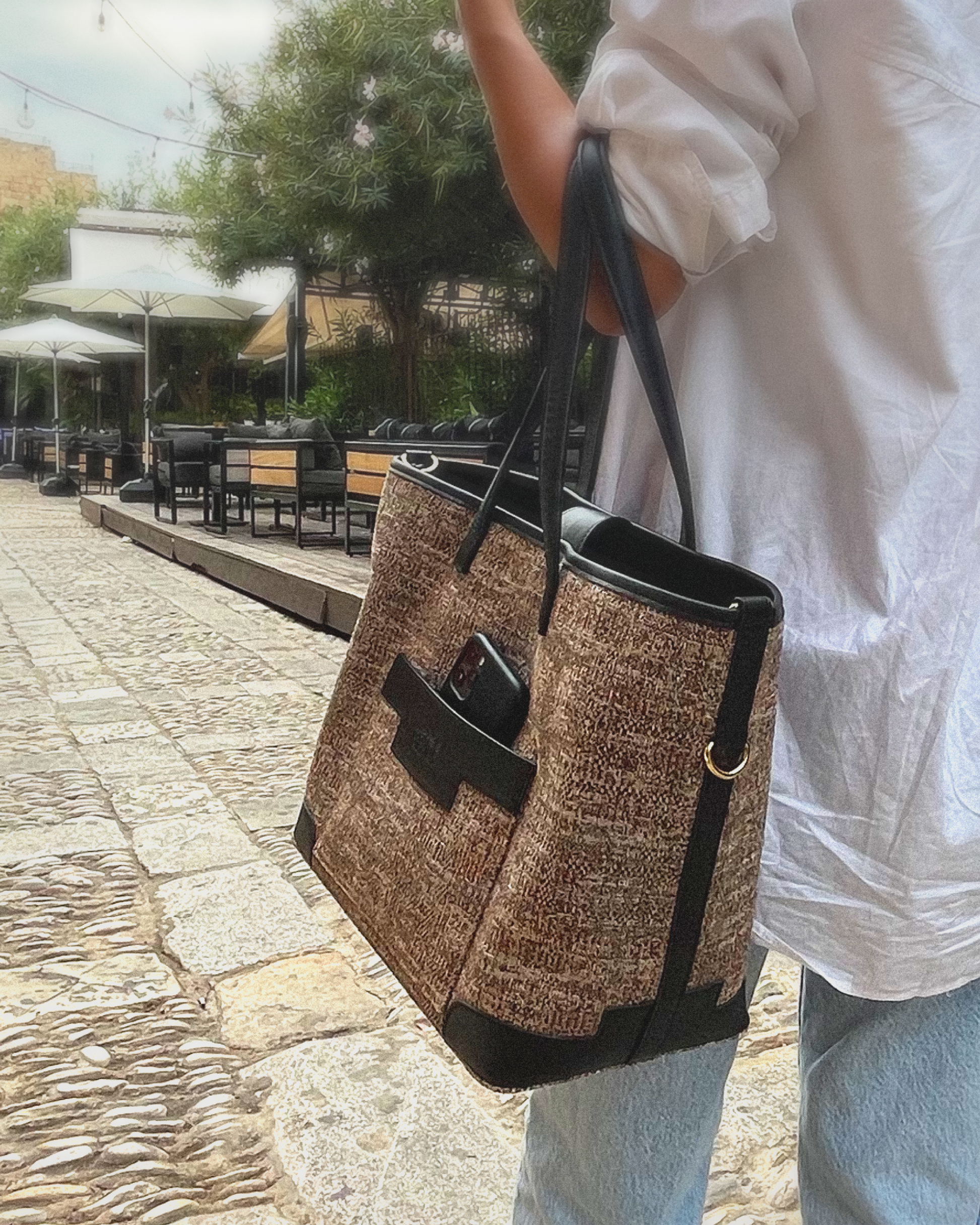 Person holding a woven large tote bag on a stone pavement