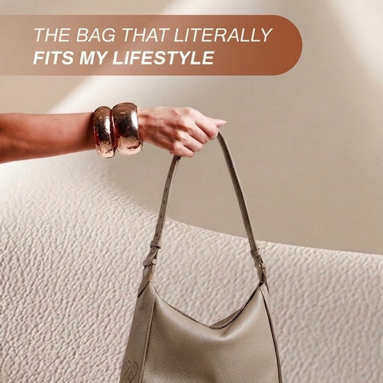 woman showing the lea shoulder bag how soft slouchy and practical it is . bag in genuine greige leather